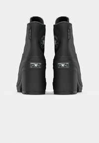 Bottines noires imperméables à talon plateforme épais, avec un bout arrondi et un détail de logo circulaire à l'arrière.