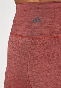 Leggings taille haute en tissu texturé bordeaux avec un logo gris foncé contrastant. Caractéristiques d'une finition lisse et de coutures renforcées.