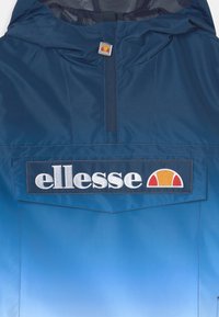Chaqueta de sudadera con capucha en azul marino y degradado en teal, que presenta un destacado logo de "ellesse" y una insignia redonda con acentos de color en el pecho.