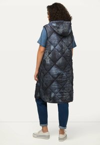 Gequiltete, dunkelblaue ärmellose Weste mit Kapuze, die ein Rautenmuster aufweist, zwei seitliche Taschen und eine leicht strukturierte Oberfläche hat.