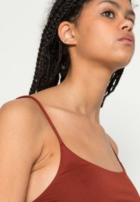 Camisola de cor ferrugem com alças finas, feita de tecido suave, apresentando um design ajustado e um decote minimalista.