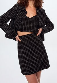 Ensemble deux pièces à carreaux noirs comprenant un haut court et une jupe ajustée avec une veste assortie, en tissu texturé et avec des motifs accentués en argent.