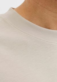 T-shirt en coton beige clair présentant un col rond avec une finition texturée et des coutures visibles, mettant en valeur la douceur du tissu.