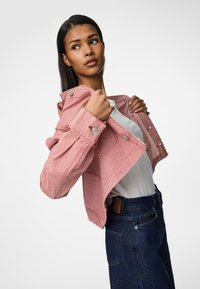 Vörös és fehér csíkos cropped dzseki patent gombokkal, fehér ing fölött viselve, sötétkék magasderekú farmernadrággal párosítva.