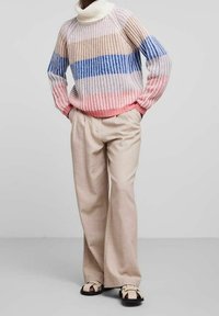 Stickad tröja med hög hals, med ränder i rosa, blått och vitt. Tillsammans med lösa beige byxor och svarta sandaler.