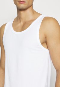 Top blanco sin mangas, de material de algodón, diseño sin mangas, escote redondeado, textura suave, forma ajustada, estilo minimalista.