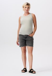 Ljust grå ärmlös tröja med ribbad textur, matchad med mörkgrå denimshorts och svarta sandaler. Modellen står med ena handen i fickan.
