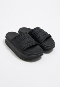 Chanclas negras con suelas gruesas y correas anchas grabadas con el texto "BIMBA Y LOLA", mostradas sobre un fondo blanco.