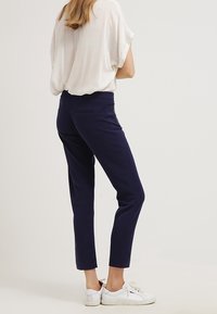 Navy pantalon in slim fit, met een gladde textuur en zijzakken, gecombineerd met een losse witte top en witte sneakers.