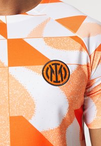 Camisa de manga corta naranja y blanca con patrones geométricos abstractos y un logotipo bordado en negro en el pecho.