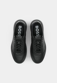 Zapatilla negra hecha de cuero suave. Presenta cordones cerrados, puntera redondeada y plantilla con logo. Diseño minimalista con una suela de goma gruesa.