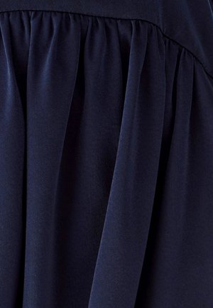 Tamnoplava tkanina s mekanom teksturom, s naborima koji stvaraju tekući dizajn. Materijal izgleda gladak i lagan.