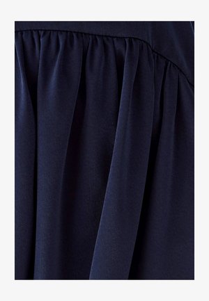 Tamnoplava tkanina s mekanom teksturom, s naborima koji stvaraju tekući dizajn. Materijal izgleda gladak i lagan.