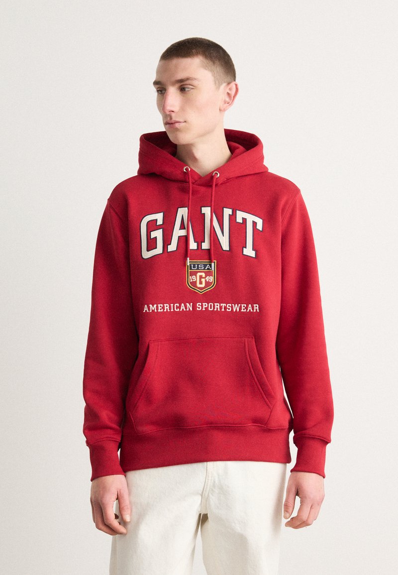 Sudadera roja de algodón, con un bolsillo frontal, capucha con cordón y texto impreso que incluye "GANT" y "AMERICAN SPORTSWEAR."