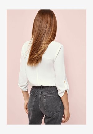 Bela srajca s tremi četrtinami rokavov, s šivo na hrbtni strani. Pairs z visokimi sivimi jeans hlačami, ki imajo dve zadnji žepki.