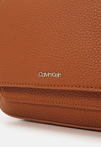 Calvin Klein braune strukturierte Lederbrieftasche mit goldfarbenem Logodetail, verziert mit gesteppten Akzenten und einem glatten, strukturierten Design.