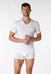 T-shirt bianco a collo a V con maniche corte e boxer bianchi aderenti. Entrambi i capi sono realizzati in un tessuto liscio e leggero.