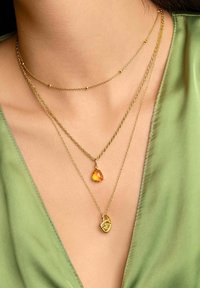 Trois colliers en or. L'un possède une pierre en ambre en forme de goutte, un autre présente un cadenas décoratif, et le troisième a de petites perles en or.