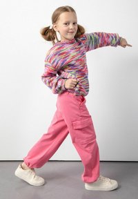 Wielokolorowy sweter dzianinowy z długimi rękawami i okrągłym dekoltem, zestawiony z luźnymi różowymi spodniami cargo z bocznymi kieszeniami.