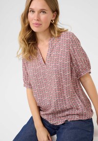 Blouse à manches courtes, coupe décontractée, dans un motif zigzag rose et gris, fabriquée en tissu léger avec un décolleté en v et des manches froncées.