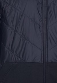 Mörkblå jacka med ett quiltat, diagonalt mönster. Dragkedjestängning, ribbade mudd och nederkant gjorda av ett smidigt, elastiskt tyg. Har sidofickor.