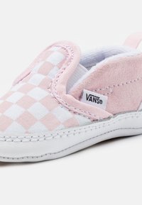 Scarpa slip-on a scacchi rosa e bianca, realizzata in tessuto e suede, con suola in gomma bianca e etichetta con logo Vans. Dettagli con texture morbida.