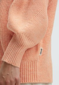 Peach-colored knitted sweater with ribbed texture, featuring puffed sleeves and a small label reading "SENSES" on the side.