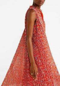 Robe sans manches rouge à fleurs avec une coupe ample, en tissu texturé, décolleté en V et motif complexe aux couleurs contrastées.