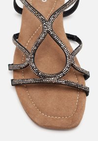 Sandalia negra con tiras, con una plantilla de ante marrón texturizada, que presenta acentos de strass brillantes en las tiras y una suela suave.
