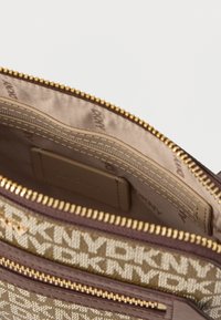 Interno di una borsa a tracolla in tela marrone e beige con un motivo a logo. Presenta una cerniera dorata e uno scomparto per carte in pelle liscia. Foderato in tessuto testurizzato.