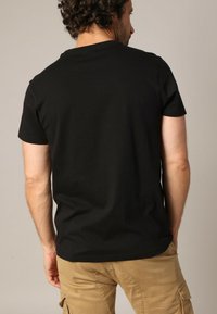 T-shirt en coton noir à manches courtes et col ras du cou ; texture lisse, design uni, avec une coupe décontractée. Couture visible à l'ourlet.