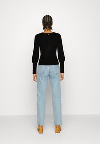 Top noir à manches longues côtelé avec un col rond, associé à un jean droit bleu clair. Le mannequin porte des sandales à talons blocs beiges.