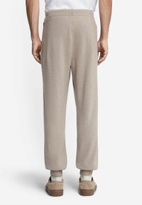 Beżowe, miękkie spodnie dresowe z prostym krojem nogawek, elastycznym paskiem w talii, prążkowanymi mankietami na kostkach i gładkim, teksturowanym wykończeniem.