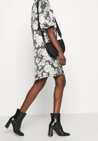 Sukienka w kwiatowy wzór w czerni i bieli, krótki rękaw z detalem bufki, w komplecie z błyszczącymi czarnymi botkami na kostkę i małą torebką na ramię.