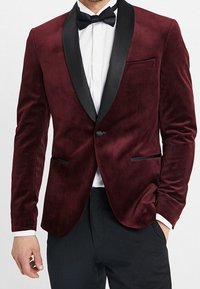 Głęboki burgundowy żakiet z aksamitu z czarnymi satynowymi klapami, jednobutonowy zamek i dwie przednie kieszenie. Gładka tekstura, dopasowany krój.