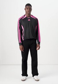 Juodas ilgomis rankovėmis sportinis marškinėlis su rožinėmis akcentais ir trimis rožinėmis juostelėmis ant pečių, derinamas su juodomis kelnėmis ir baltomis sportbačiais.