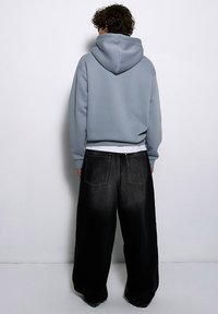 Szara bluza z kapturem o luźnym kroju w połączeniu z oversize'owymi czarnymi dżinsami o wyblakłym wykończeniu i tylnymi kieszeniami.