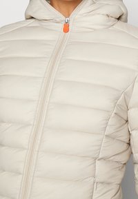 Hellbeige Puffermantel mit einem Reißverschluss auf der Vorderseite, Kapuze und orangefarbenem Reißverschluss-Zipper. Mit horizontalen Steppabschnitten und glatter Textur.