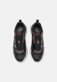 Fekete sneaker hálós anyaggal, barna díszítéssel és sima felülettel. Vastag fehér talppal és húzófüllel a könnyű felvétel érdekében.