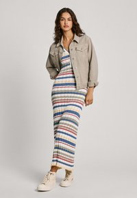 Abito maxi a righe con colori blu, rosso, verde e crema; presenta un corpetto aderente e una gonna fluida e svolazzante. Abbinato a un giaccone grigio chiaro.