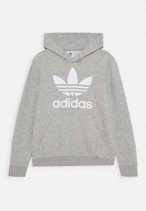 Jasnoszara bluza Adidas z kapturem, z przednią kieszenią typu kangur, dużym białym logo koniczyny i nazwą marki na piersi, długimi rękawami oraz przymocowanym kapturem.