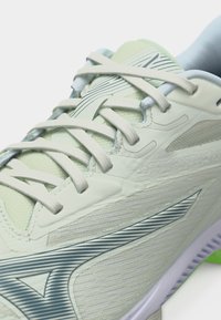 Κοντινό πλάνο αθλητικού παπουτσιού ανοιχτού πράσινου χρώματος με λευκά κορδόνια και σκούρο ριγωτό λογότυπο στην υφασμάτινη πλαϊνή πλευρά.