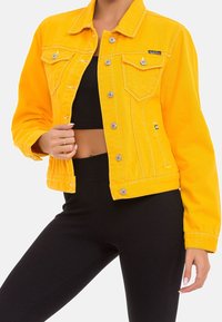 Yellow denim jacket with silver buttons, two front pockets, and a fitted design, paired with black ribbed leggings.