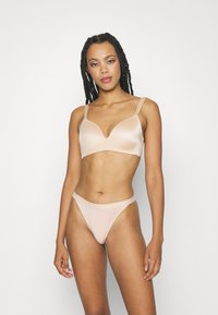 Nude satin bra with a plunging V-neck and adjustable straps, paired with matching minimalistic thong underwear in a similar shade.