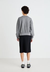 Sweatshirt cinza de algodão com ombros caídos e bainha canelada, combinado com uma saia preta até ao joelho. O calçado notável apresenta ténis pretos.