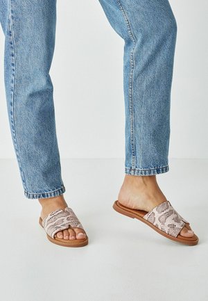 Leather slide sandals in light pink with a snakeskin pattern. Flat sole with open toe and side cutouts, paired with blue denim jeans.