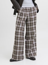 Weite Karottenhosen in Braun, Weiß und Creme, mit weichem Material und elastischem Bund. Kombiniert mit einer schwarzen Lederjacke.