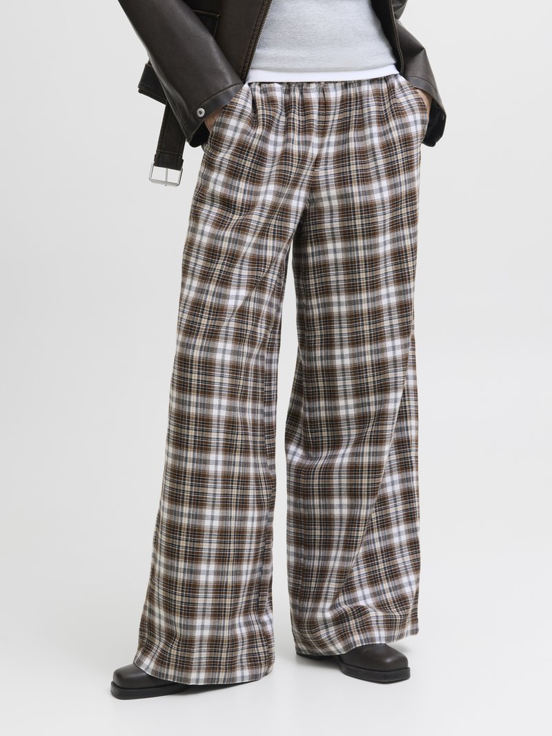 Weite Karottenhosen in Braun, Weiß und Creme, mit weichem Material und elastischem Bund. Kombiniert mit einer schwarzen Lederjacke.
