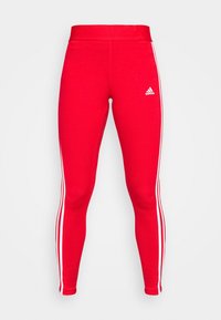 Czerwone legginsy sportowe o dopasowanym kroju, wykonane z elastycznego materiału, z białymi paskami po bokach i małym białym logo na talii.