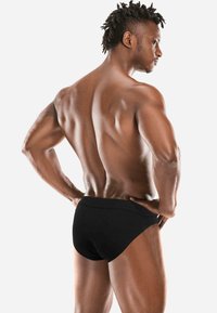 Schwarze Schwimmshorts mit einem schlichten Design, das eine glatte Textur und einen bequemen Gummibund aufweist, getragen von einem fitten männlichen Modell aus der Rückansicht.